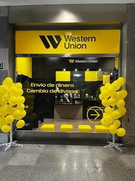 Fachada de una oficina de Western Union con logo amarillo y negro, decorada con globos. Anuncia envío de dinero