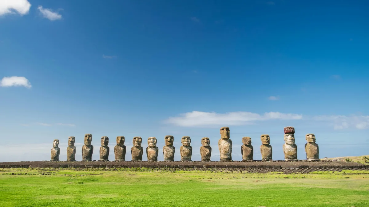 Los 15 Moai de Ahu Tongariki en Rapa Nui, Chile, sobre un campo verde bajo cielo azul. Uno luce un sombrero rojo