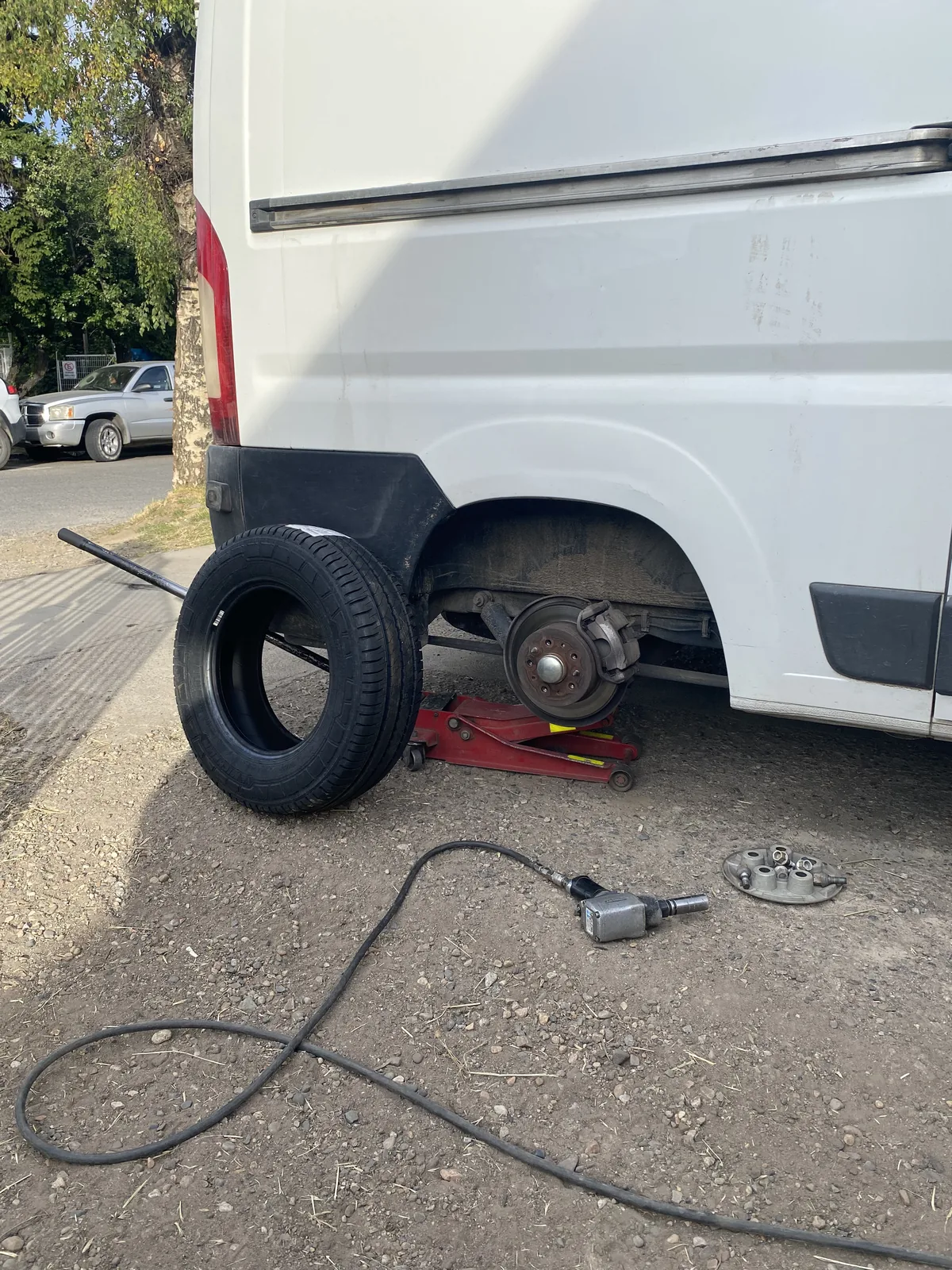 Cambio de neumático trasero en furgoneta camper blanca elevada con gato hidráulico, con pistola neumática en el suelo