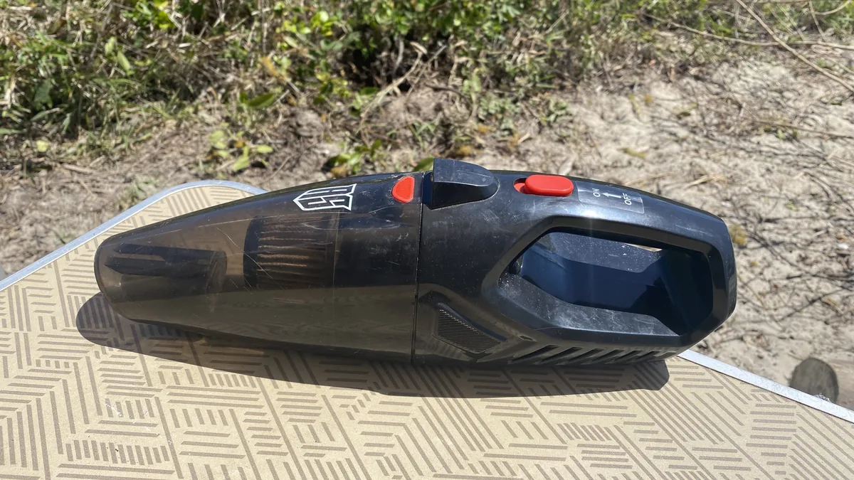 Aspiradora de mano RS negra sobre mesa de camping, perfecta para limpiar la van en viajes overland