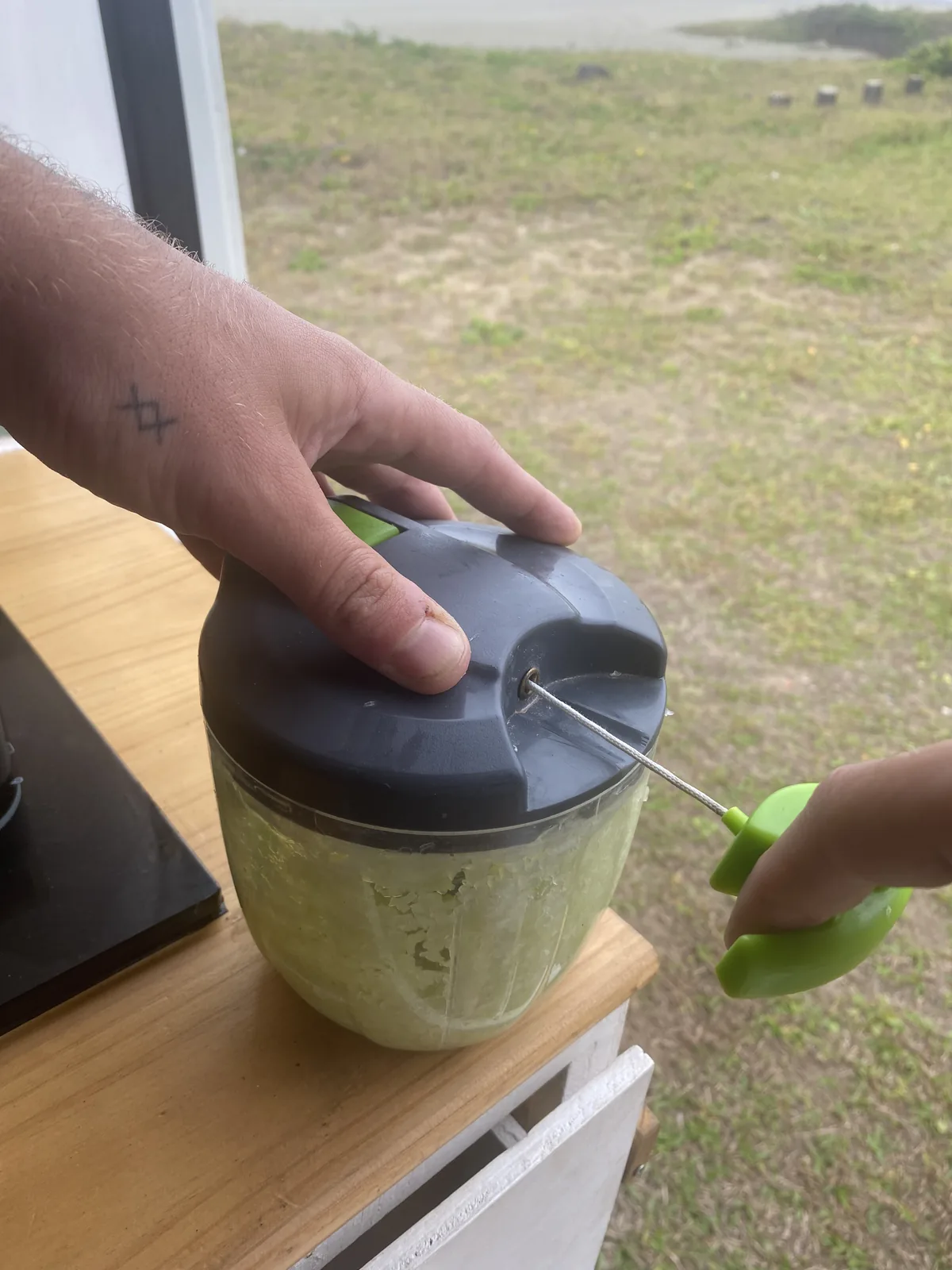 Picando verduras en un mini chopper manual dentro de la van, con vista al verde paisaje costero overland