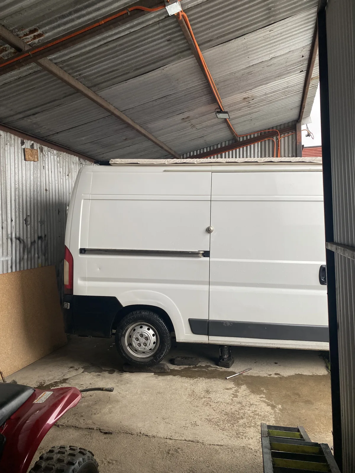 Furgoneta camper blanca levantada con gato en taller con techo de chapa, preparándose para aventuras overland