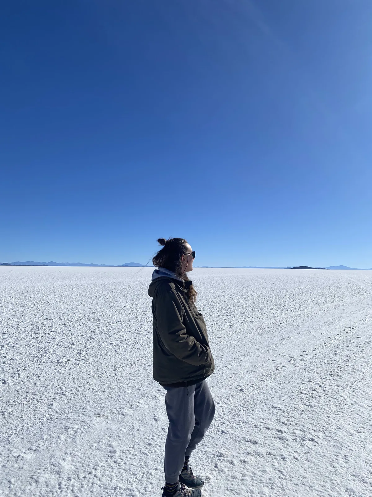 Viajera overland en el vasto Salar de Uyuni, Bolivia, con chaqueta y gafas de sol, bajo un intenso cielo azul