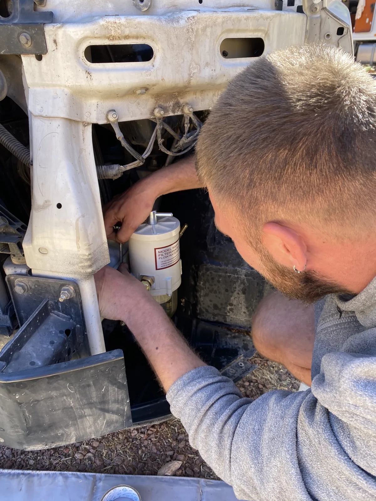 Hombre instalando filtro de combustible en el motor de una furgoneta overland, preparando el vehículo para el viaje