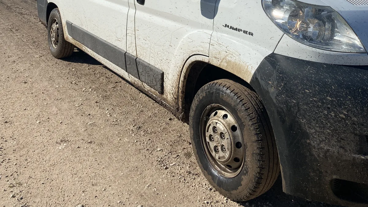 Furgoneta Citroën Jumper camper blanca cubierta de barro y polvo en un camino de tierra, un día de aventura overland