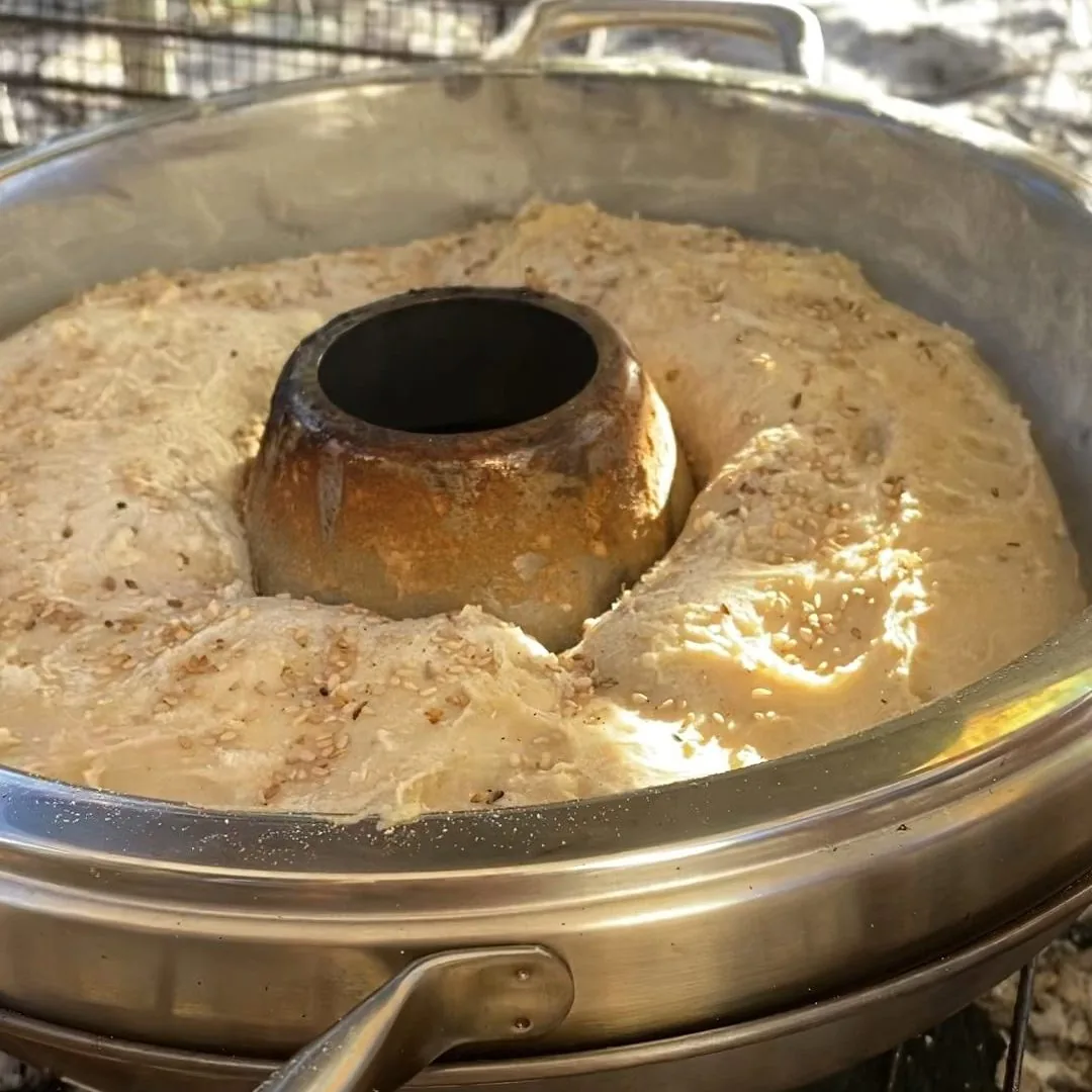 Masa de pan con sésamo leudando en olla holandesa, lista para hornear en cocina exterior durante una aventura overland
