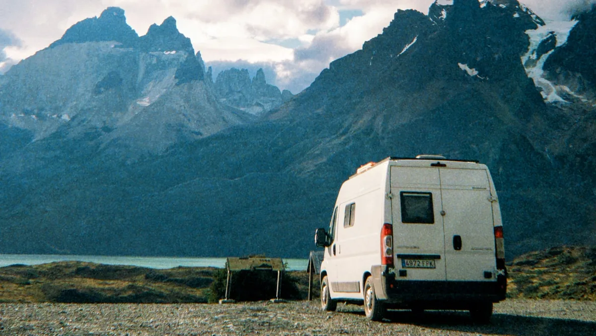 Furgoneta camper blanca en una aventura overland, aparcada frente a un lago y las espectaculares cumbres patagónicas nevadas