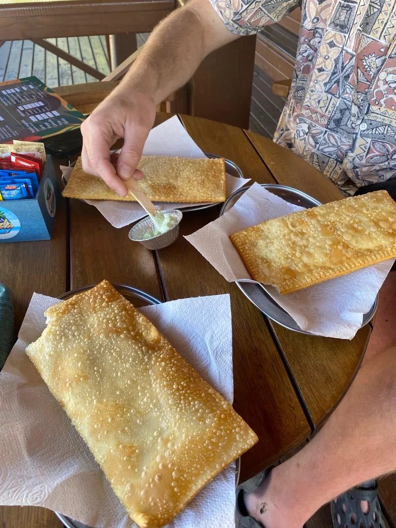 Comida típica de Brasil: tres crujientes pastéis dorados con salsa, disfrutados en una mesa de madera durante un viaje