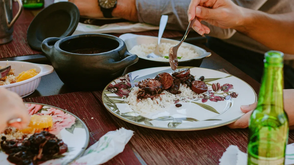 Compartiendo feijoada brasileña con arroz y farofa en platos florales, con una olla de barro y cerveza en la mesa