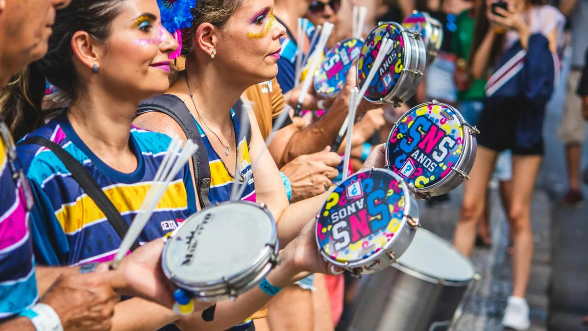 Mujeres con maquillaje festivo y camisetas de colores tocando tamborines en un alegre carnaval brasileño