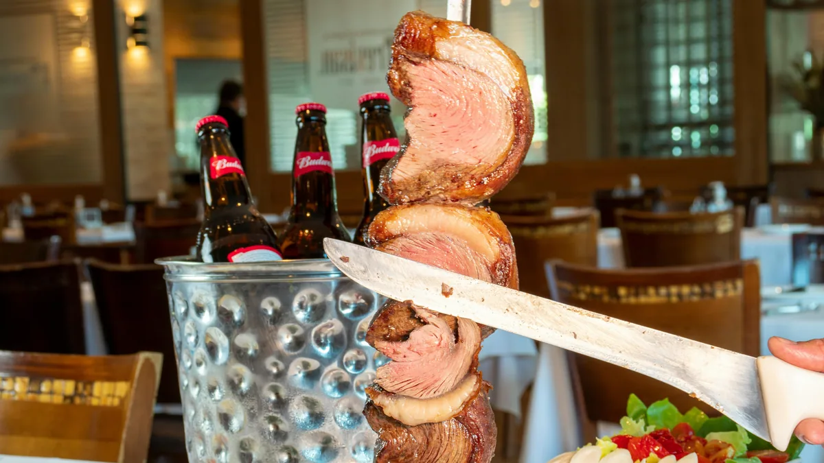 Jugosa picanha cortada del espeto en una churrasquería. Cervezas Budweiser frías en balde sobre la mesa