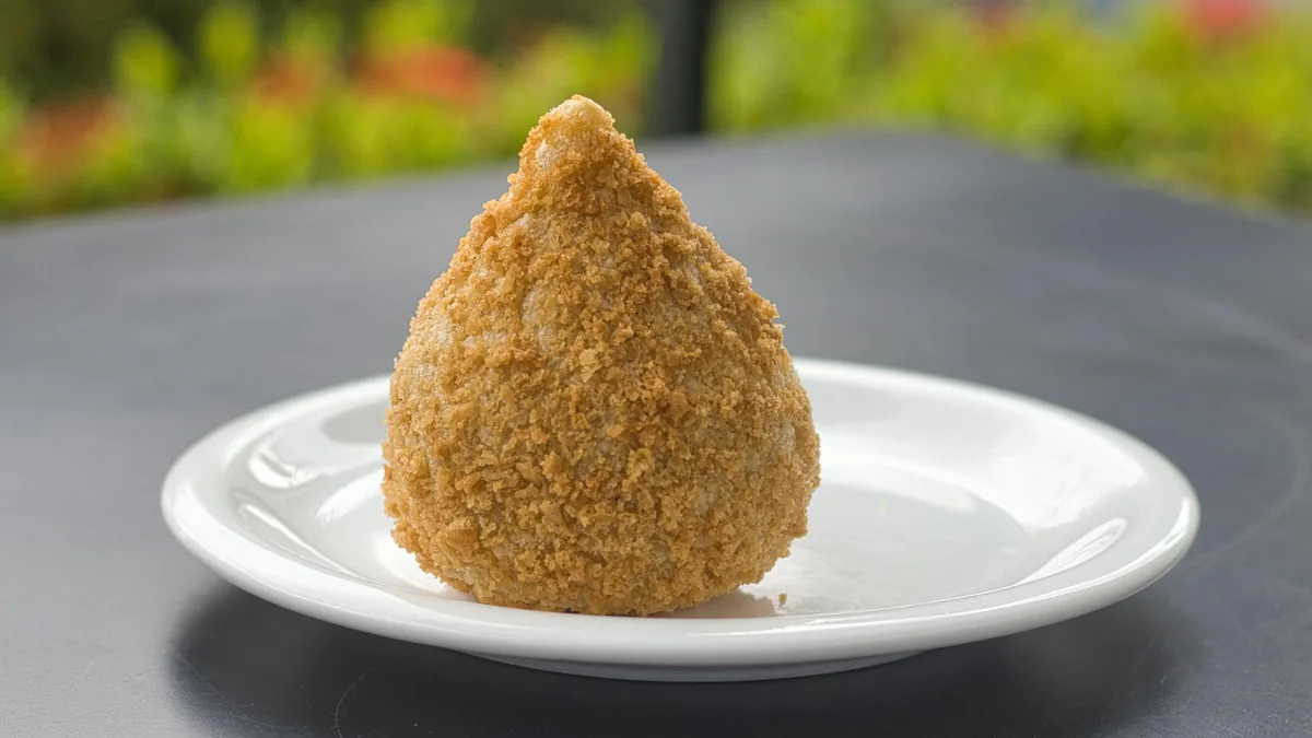 Coxinha brasileña dorada y crujiente en plato blanco, un bocado delicioso en ruta por Sudamérica