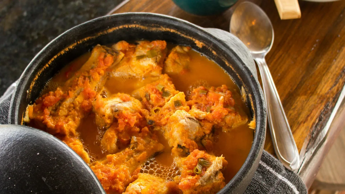 Guiso de pescado en salsa de tomate con cebolla verde, preparado en una robusta olla de hierro, perfecto para la ruta
