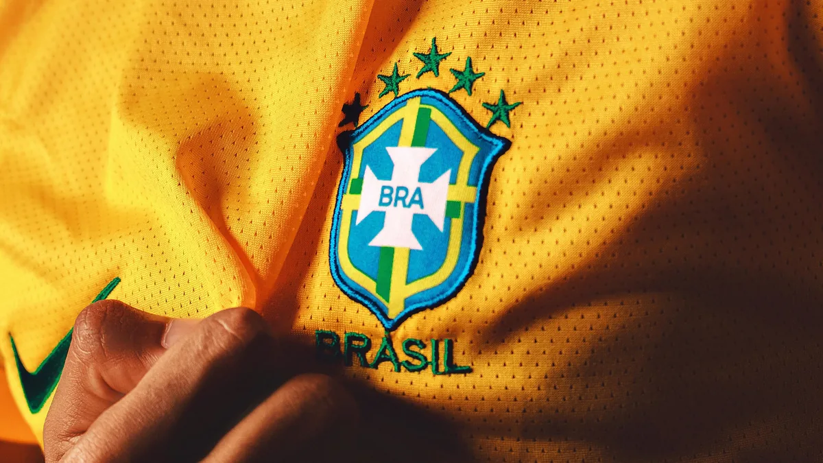Primer plano del escudo de la selección de fútbol de Brasil en camiseta amarilla, con cinco estrellas verdes y texto BRASIL