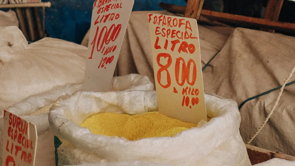 Sacos de farofa especial y otros alimentos a granel con precios escritos a mano en un colorido mercado brasileño