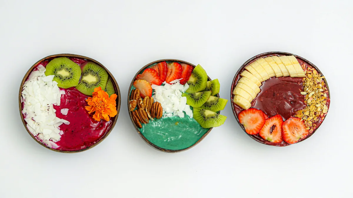 Tres bowls de smoothie en cuencos de coco con kiwi, fresas, plátano, granola, nueces y coco rallado