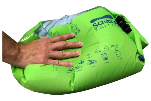 Mano presionando una Scrubba Wash Bag verde con ropa dentro, solución de lavado portátil para viajes overland