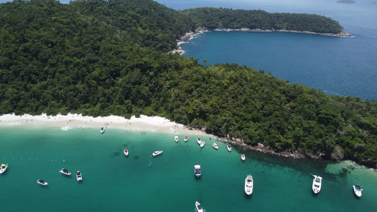 Espectacular vista aérea de una playa remota con arena blanca, frondosa selva costera y numerosas lanchas en el mar turquesa
