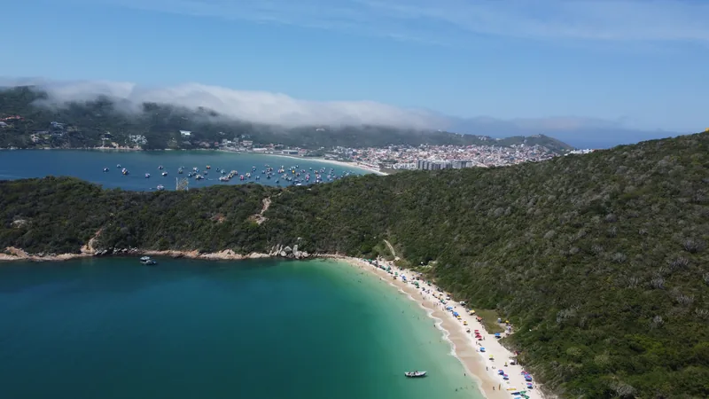 Playa con agua turquesa, arena, personas bajo sombrillas y barcos en la bahía