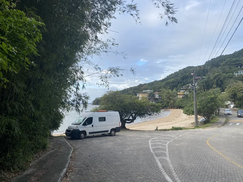 Furgoneta camper blanca con kayak naranja en el techo, aparcada en playa rodeada de naturaleza