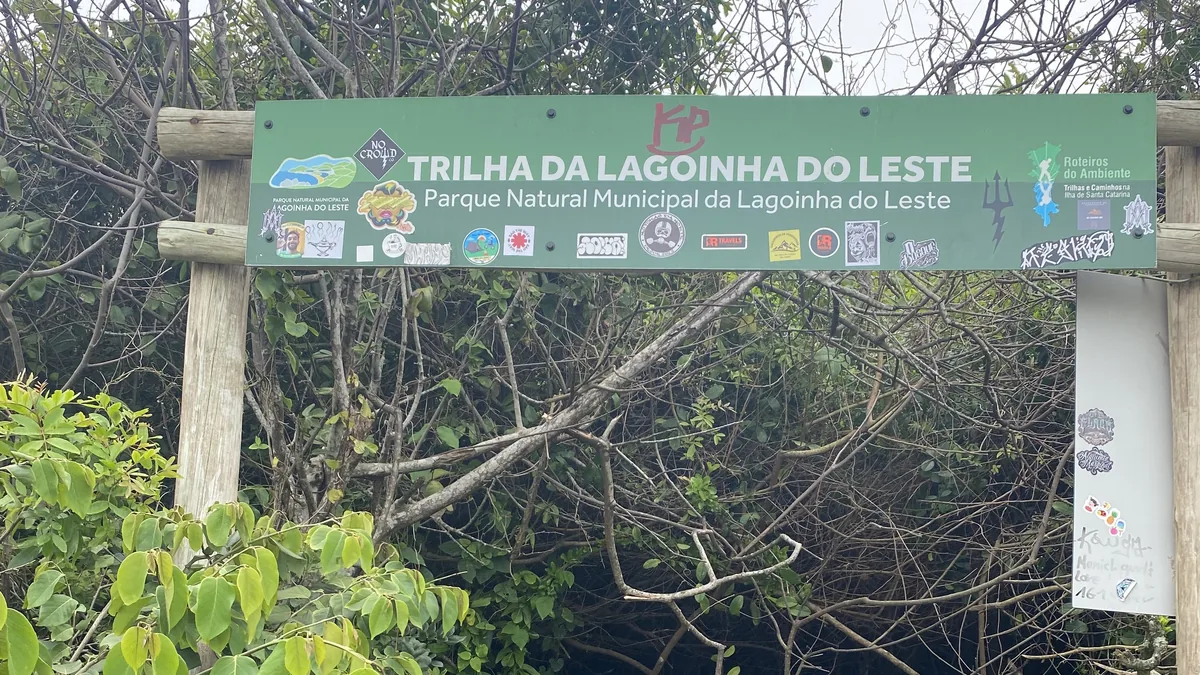 Señal de madera con la inscripción "Trilha da Lagoinha do Leste", parque natural municipal, entre frondosa vegetación