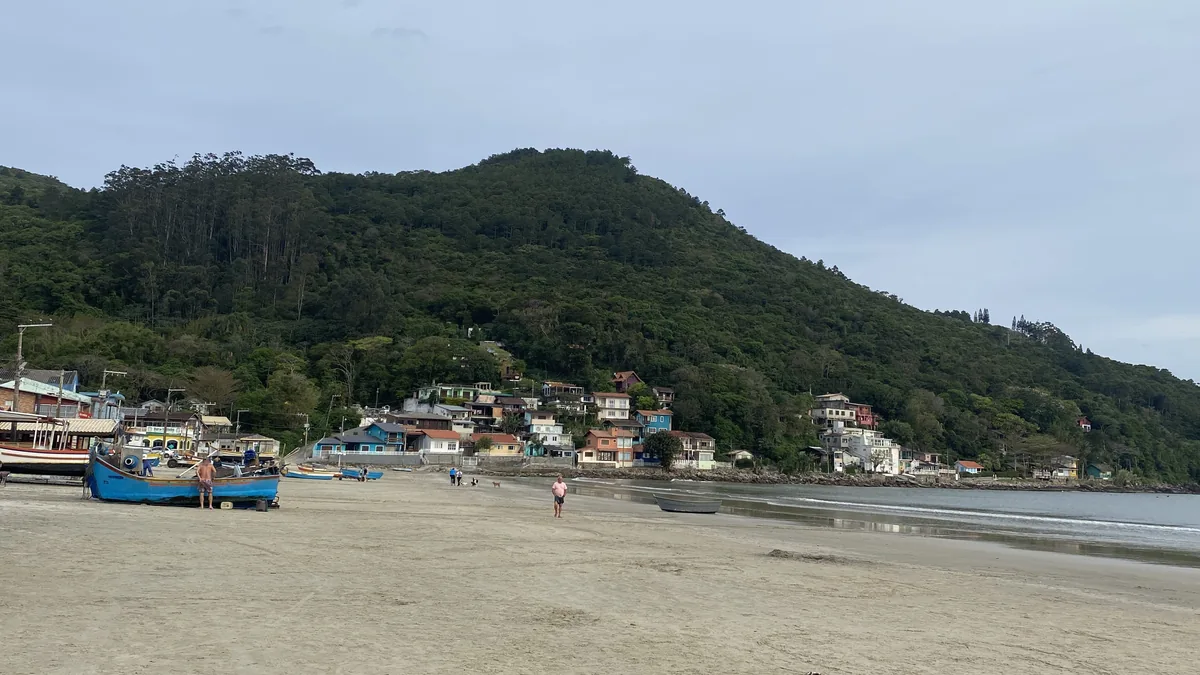 Pueblo pesquero en la costa, con casas coloridas al pie de una montaña boscosa, playa de arena y botes azules