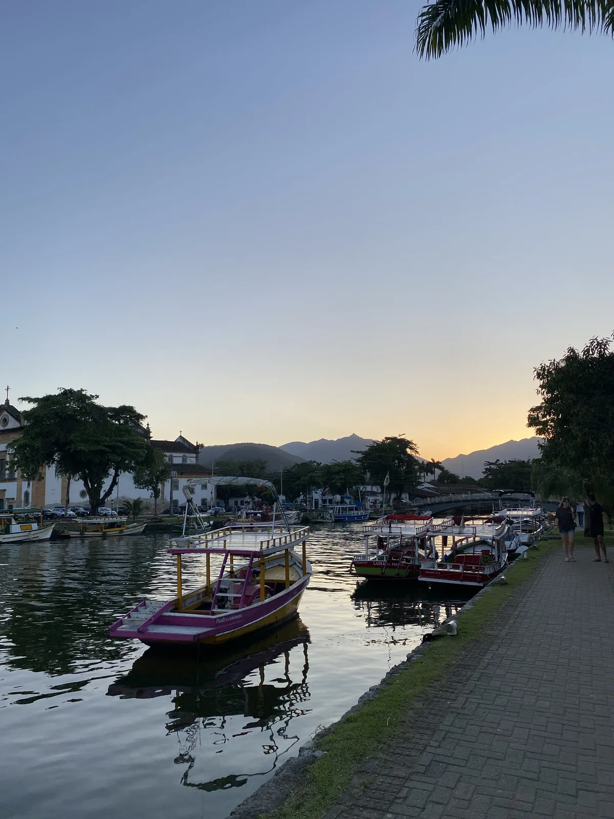 Atardecer dorado en Paraty, Brasil. Barcos de paseo coloridos en el canal, frente a iglesia colonial y montañas