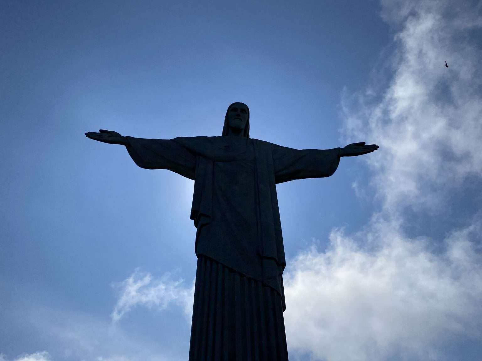 Silueta del Cristo Redentor en Río de Janeiro, Brasil, bajo un cielo azul con nubes dispersas, un ave vuela