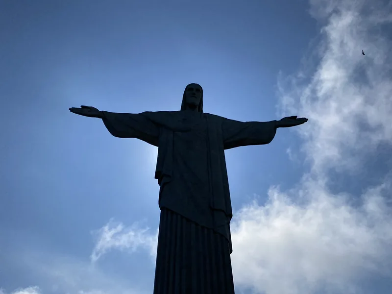 Silueta del Cristo Redentor en Río de Janeiro, Brasil, bajo un cielo azul con nubes dispersas, un ave vuela