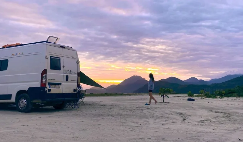 Aventura overland: furgoneta camper Citroën Jumper en una playa desierta al atardecer, con viajera disfrutando del paisaje