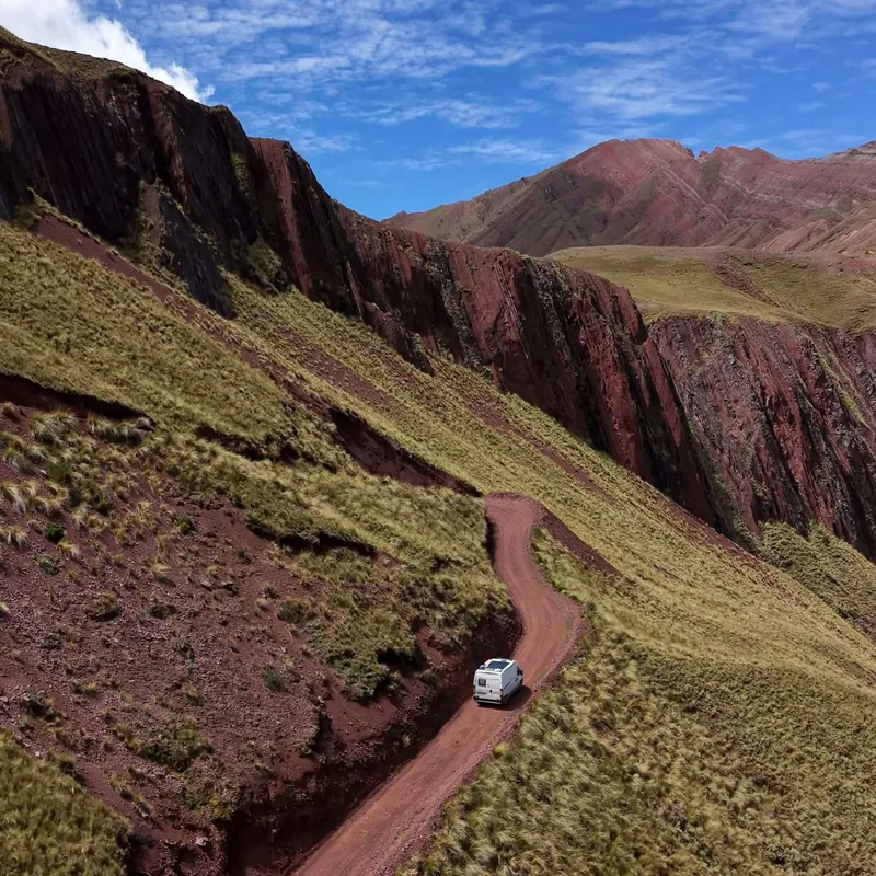Nuestra furgoneta en una pista de tierra serpenteando montañas rojas y verdes bajo cielo azul