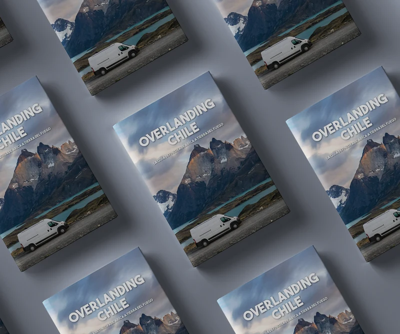 Múltiples guías de viaje apiladas, mostrando una furgoneta camper frente a montañas y un lago azul