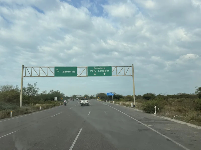Carretera con un cartel verde superior que indica 'Zarumilla' y 'Frontera Perú Ecuador