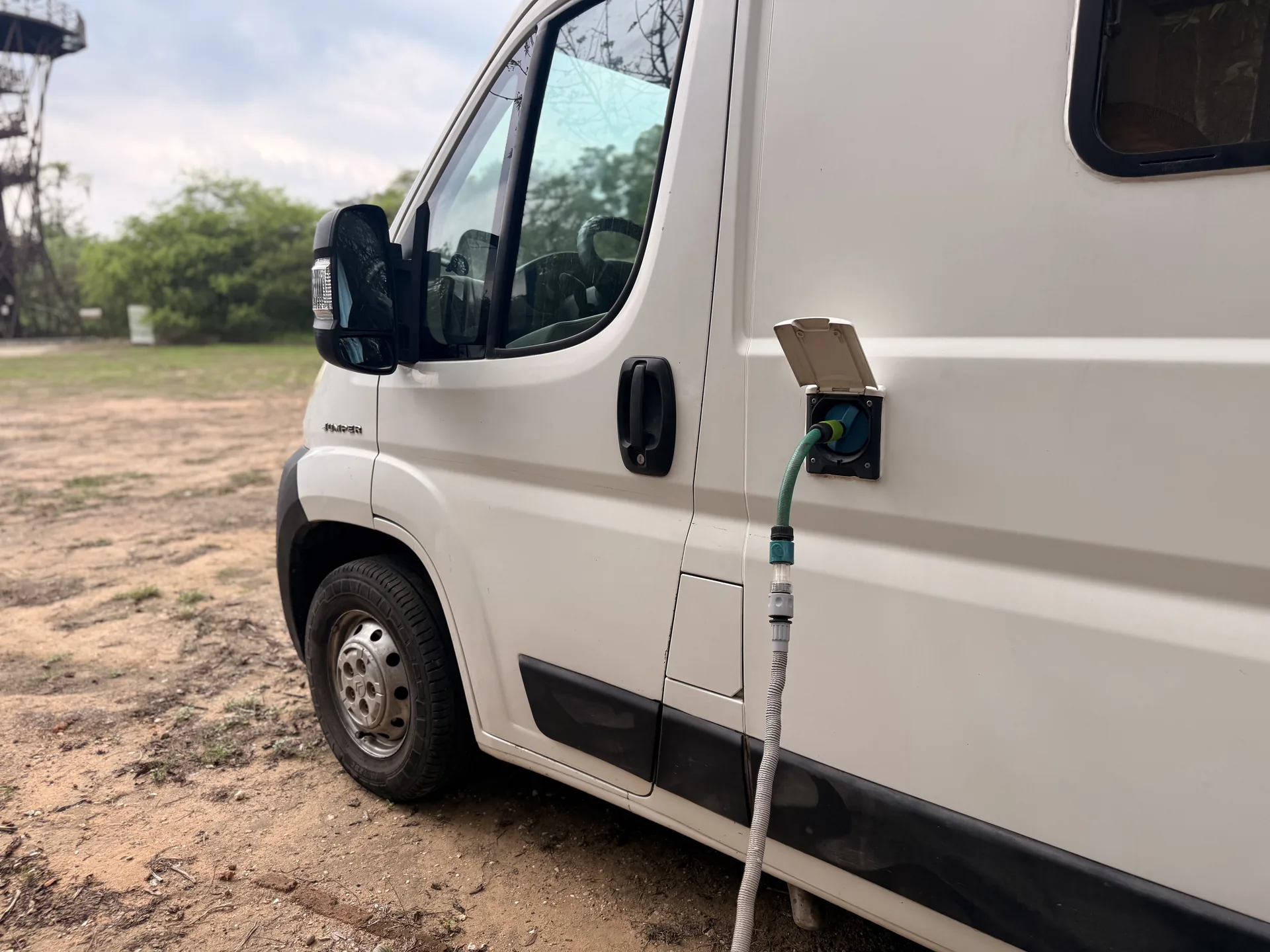 Furgoneta camper blanca cargando agua con una manguera