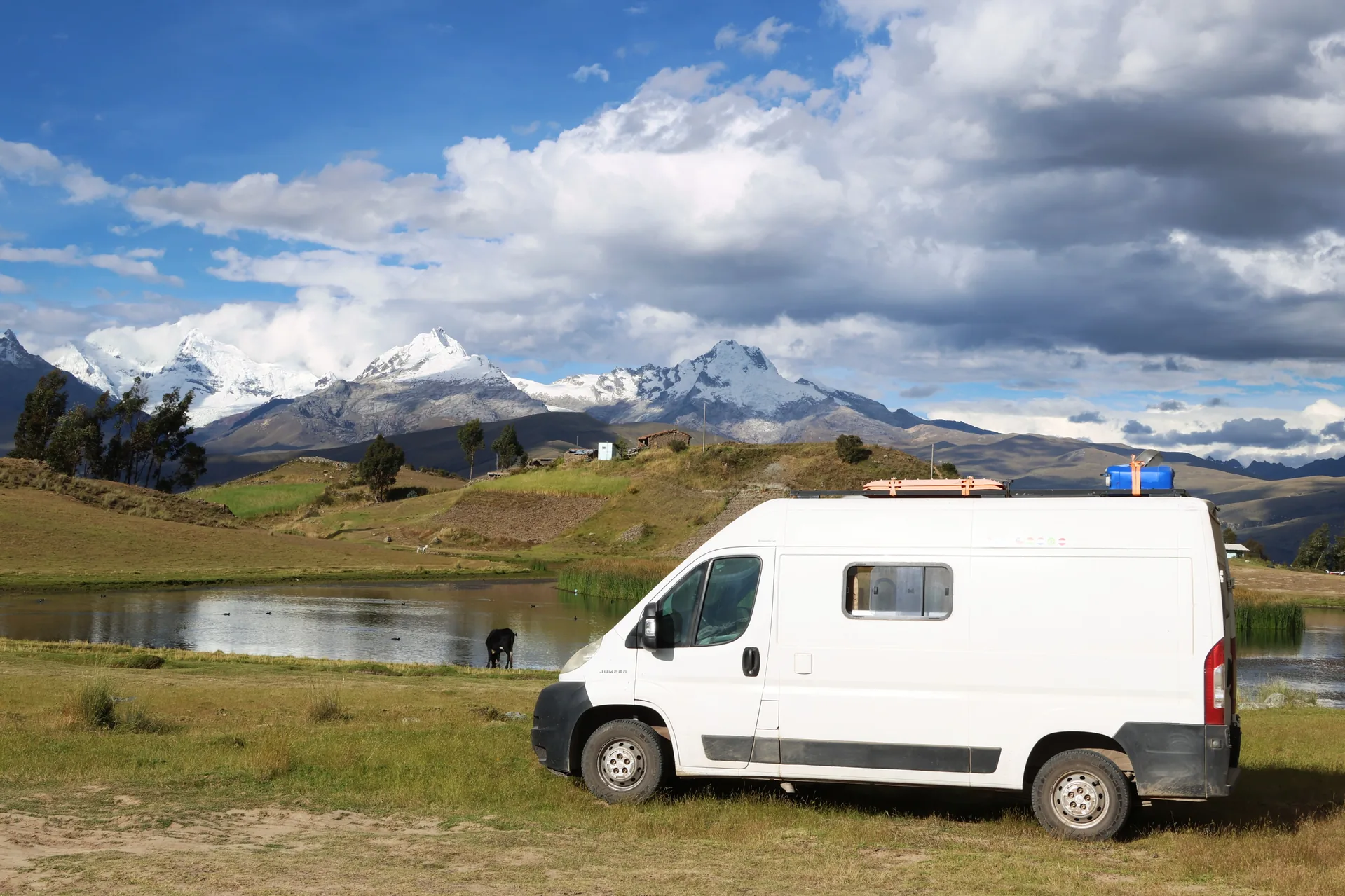 Furgoneta camper blanca en un lago con unas montañas nevadas de fondo