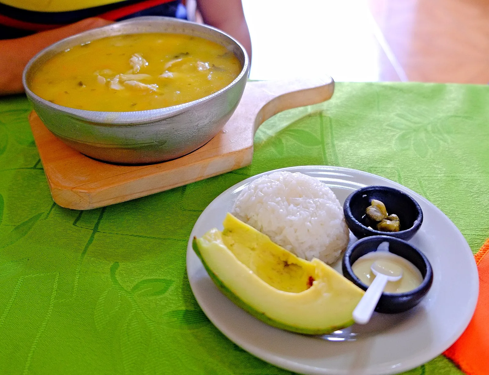 Ajiaco santafereño en cuenco con arroz blanco, aguacate, alcaparras y crema de leche