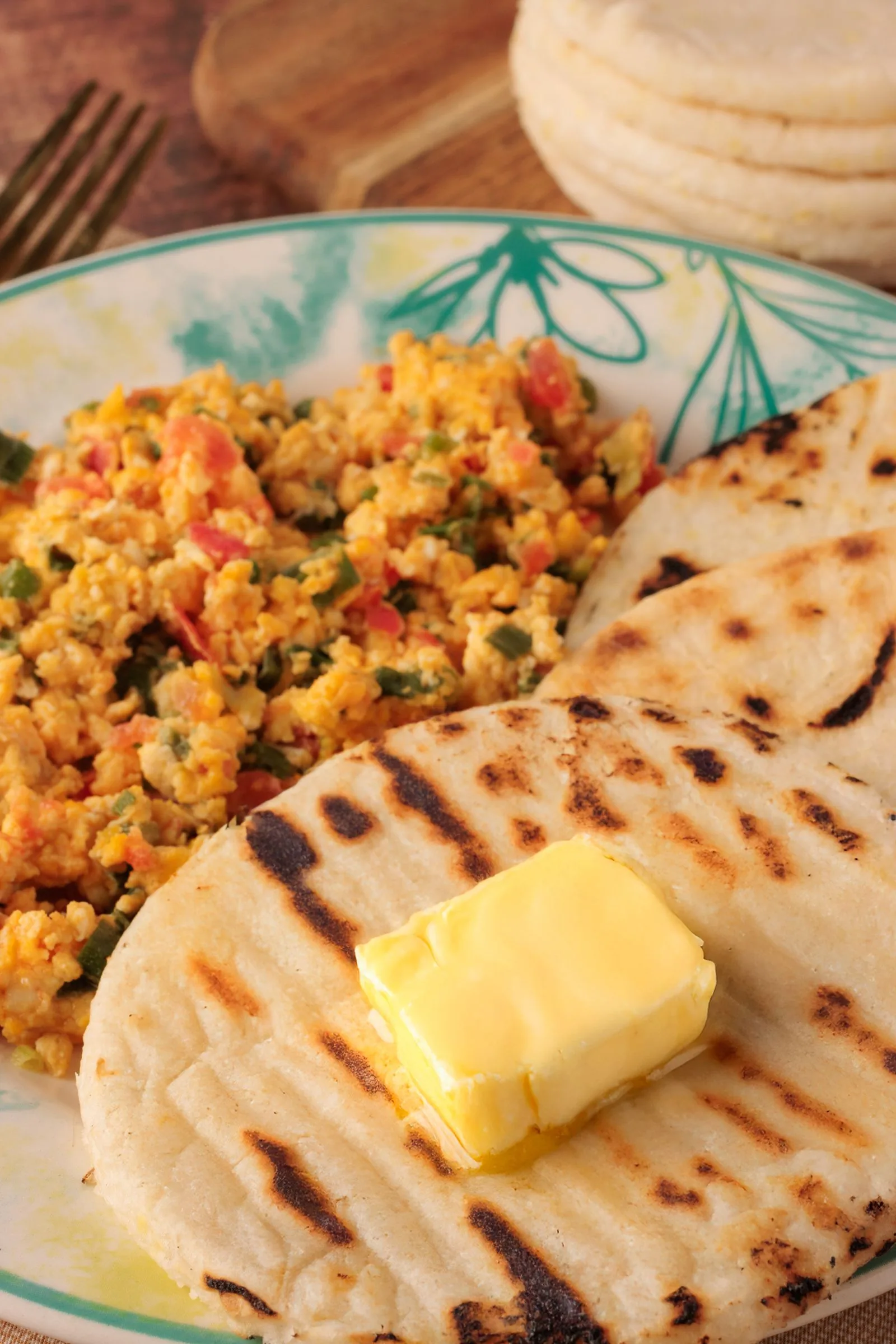 Arepa colombiana asada a la plancha con mantequilla, servida con huevos pericos