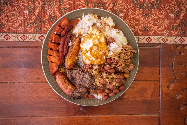 Bandeja paisa vista desde arriba con arroz, huevo frito, fríjoles, carne molida, chorizo, chicharrón y plátano maduro