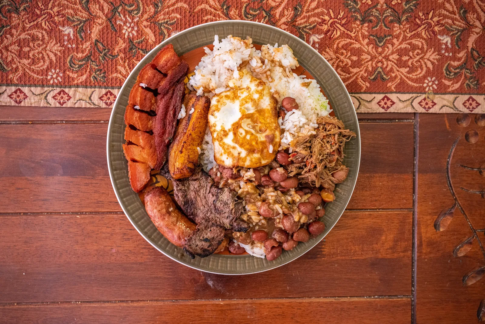 Bandeja paisa vista desde arriba con arroz, huevo frito, fríjoles, carne molida, chorizo, chicharrón y plátano maduro
