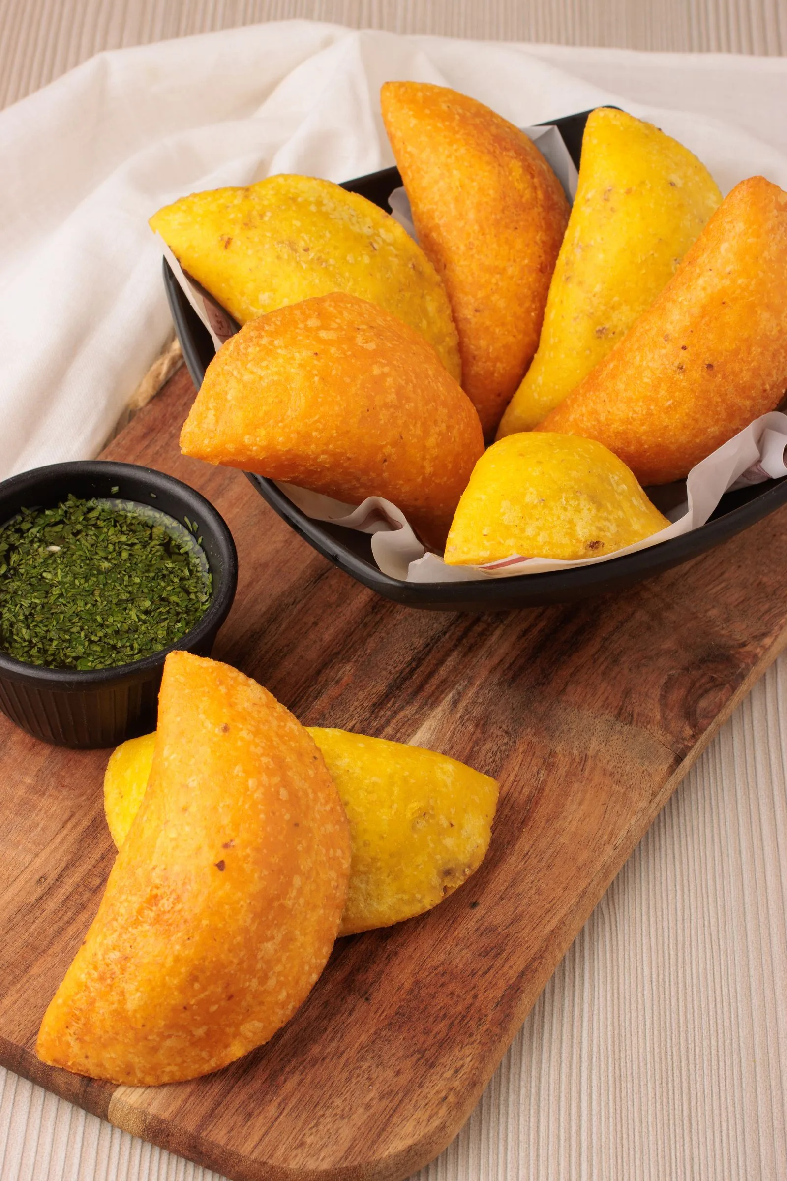 Empanadas colombianas de maíz, doradas y crujientes, con un cuenco de ají verde