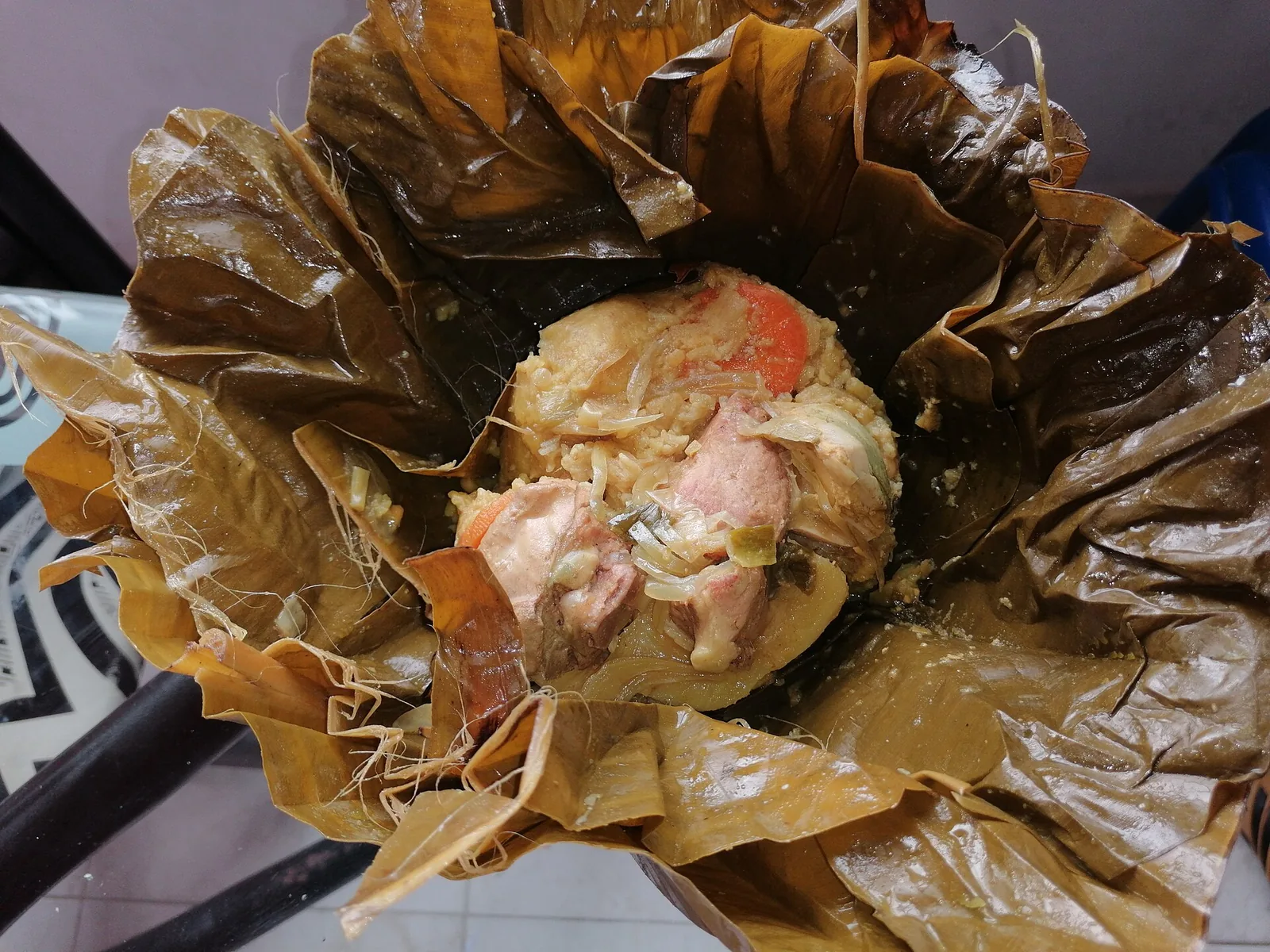 Tamal tolimense abierto sobre sus hojas de plátano, con masa, cerdo, pollo y zanahoria