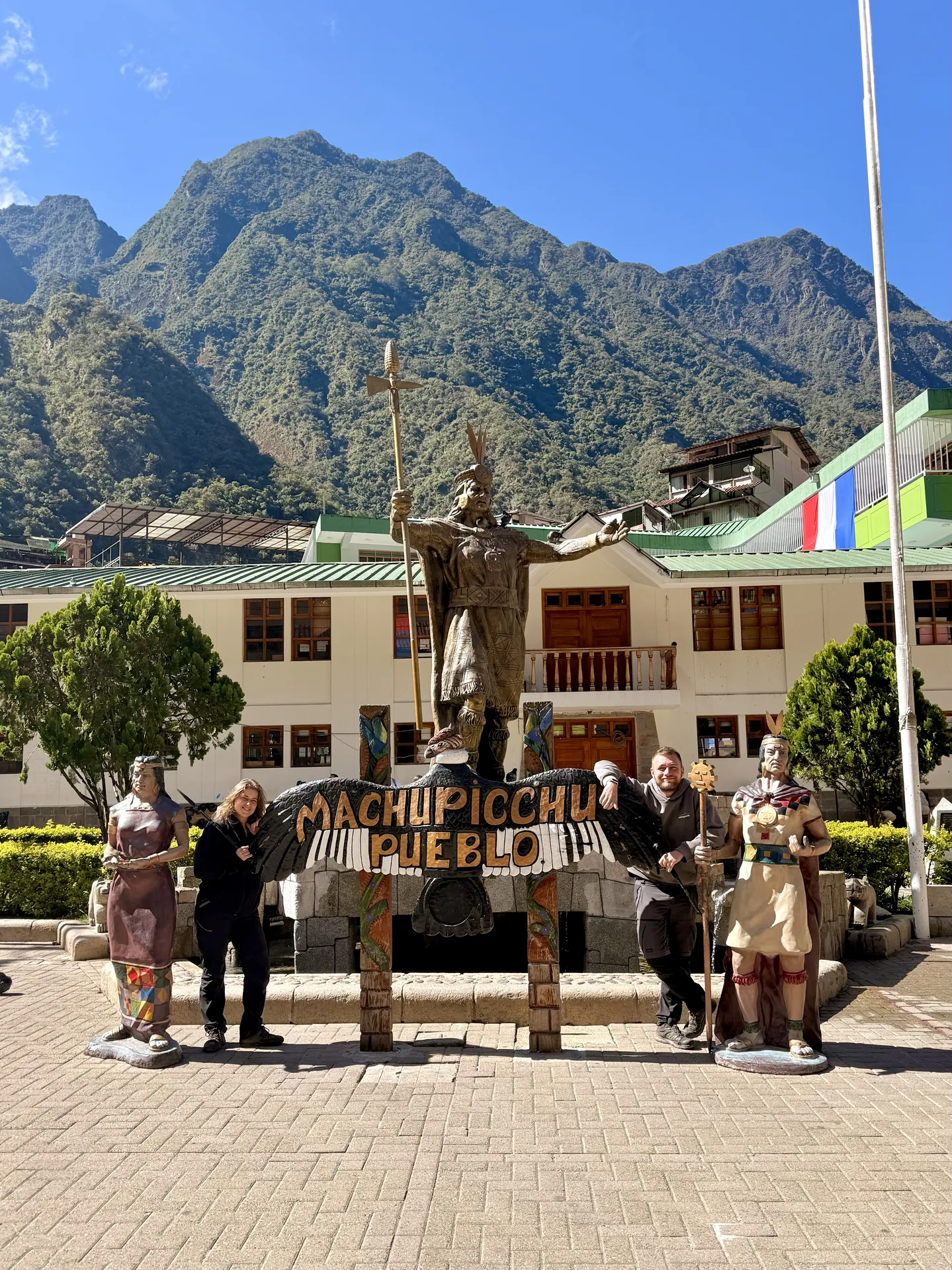 Dos personas junto al cartel de Machu Picchu Pueblo