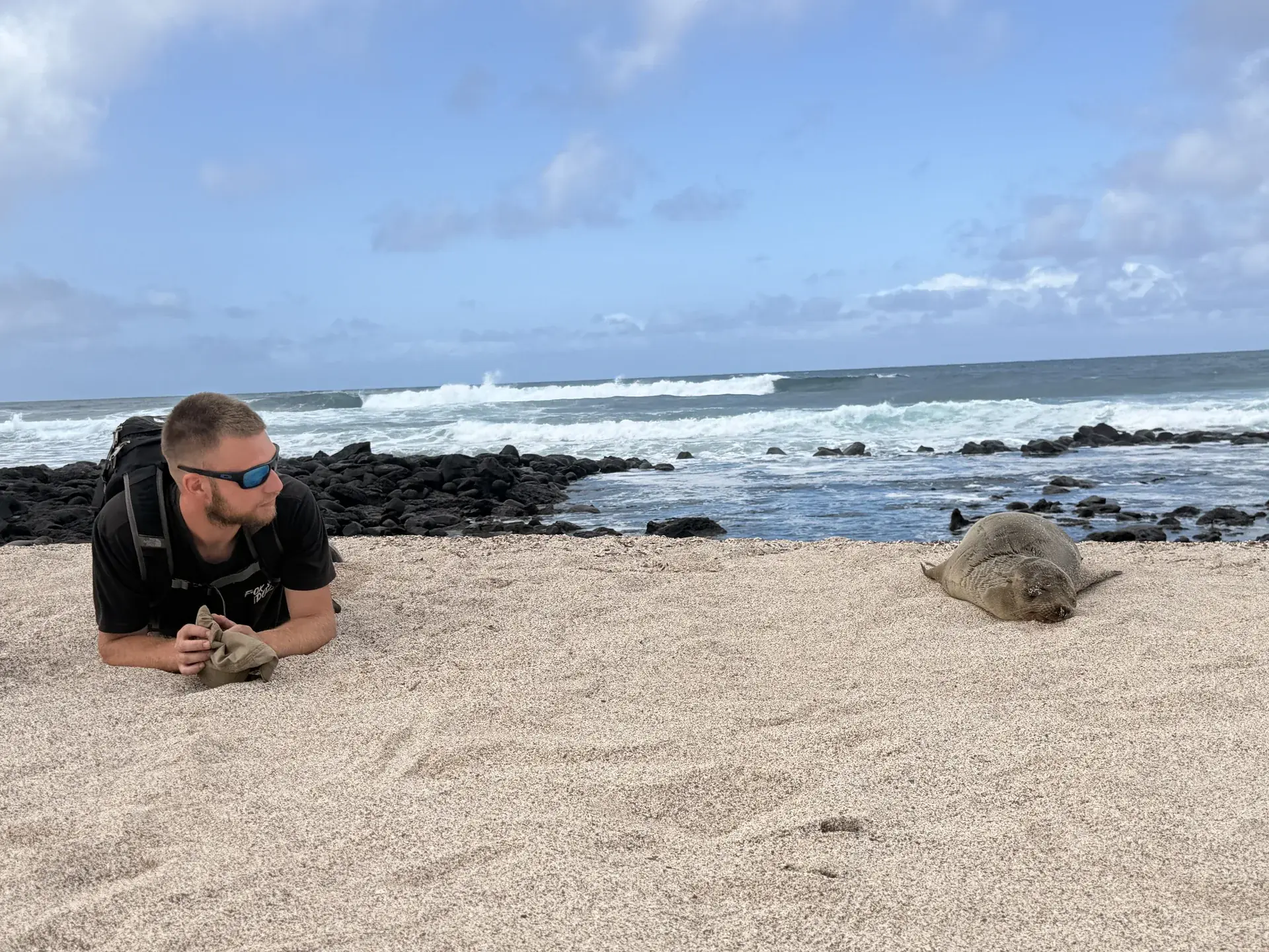 Hombre tumbado junto a un lobo marino en playa la loberia, Galápagos