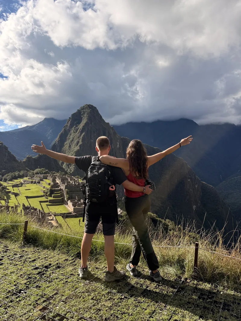 Pareja con los brazos abiertos frente a la ciudadela de Machu Picchu y la montaña Huayna Picchu