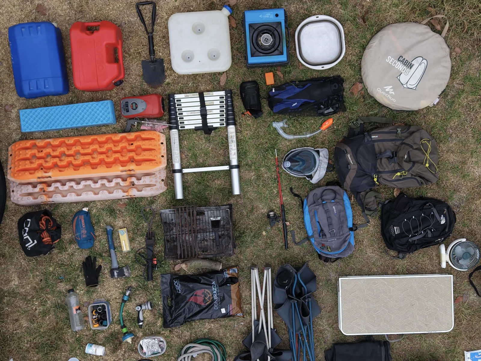 Accesorios de la furgoneta colocados sobre la hierba: placas de arena, escalera, garrafas, mochilas y sillas