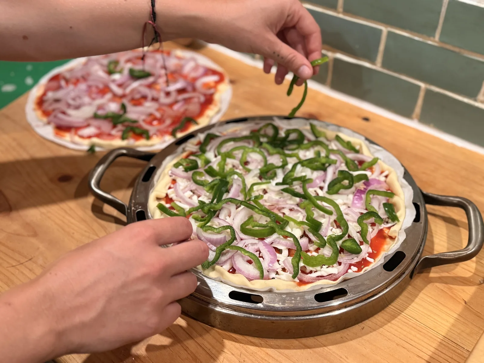 Preparando una pizza de cebolla y pimiento verde sobre una bandeja metálica, en una encimera de madera